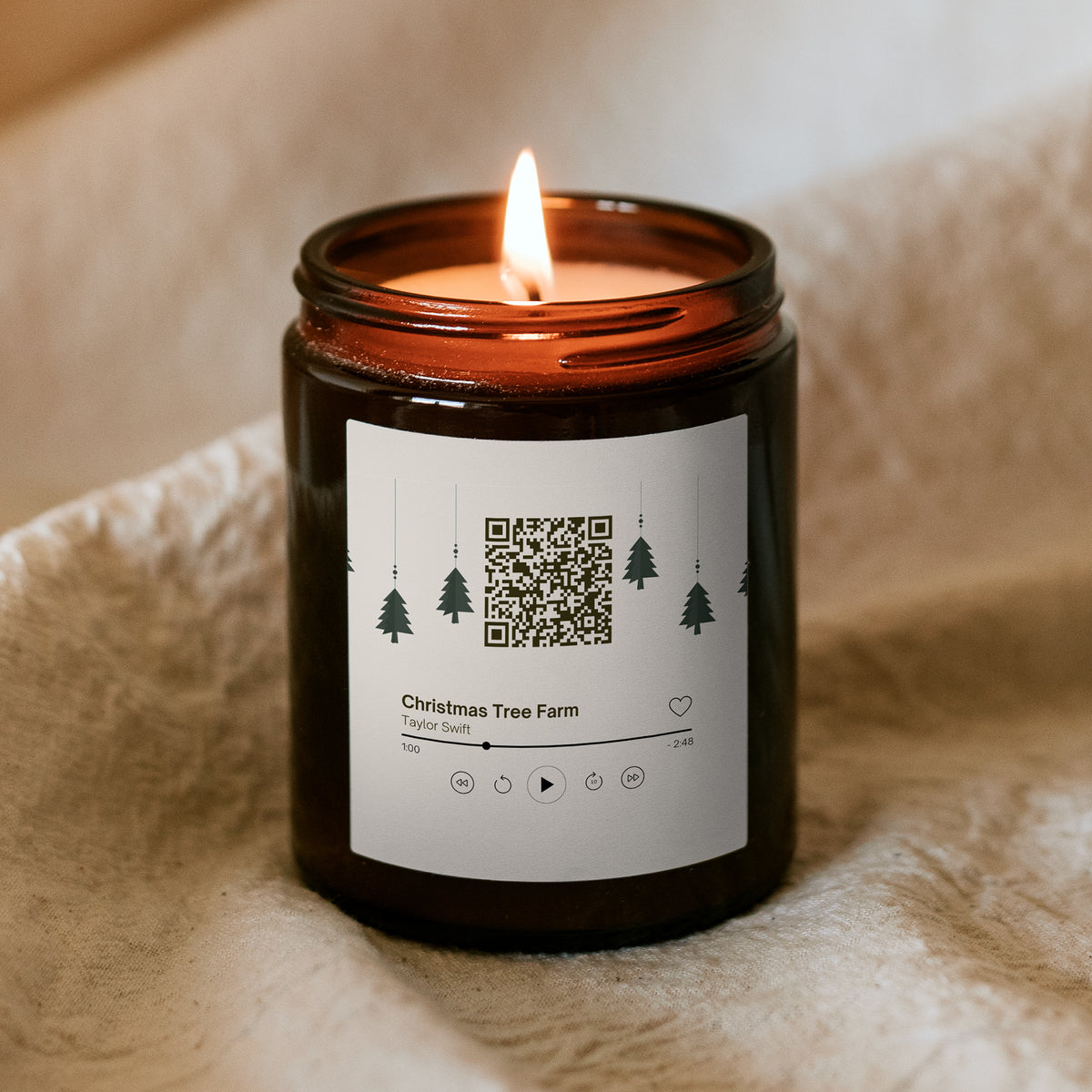 Égő Kiskedves „Dallamos” karácsonyi gyertya barna üvegtégelyben puha takarón, a címkén QR-kód és zenelejátszó-kártya a Christmas Tree Farm dallal