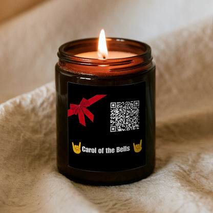 Égő Kiskedves „Dallamos” karácsonyi gyertya barna üvegtégelyben puha takarón, fekete címkén piros masni, QR-kód és a Carol of the Bells felirat rock kézjelekkel